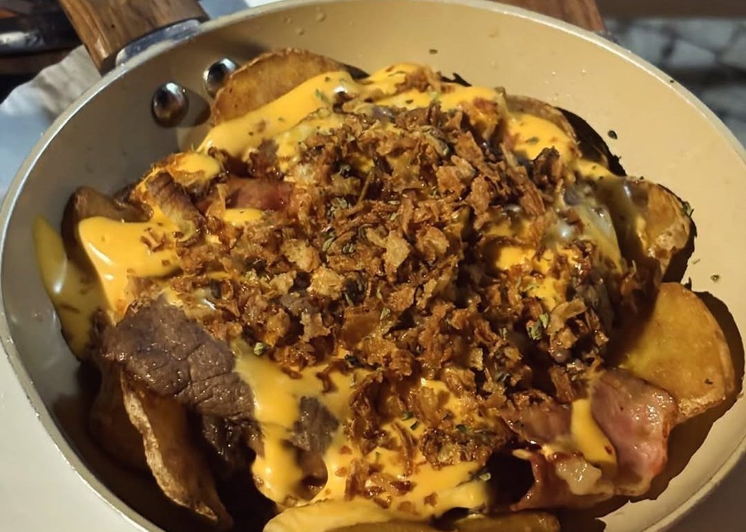 Frigideira com batatas, carne e molho gratinado, coberta de cebola frita